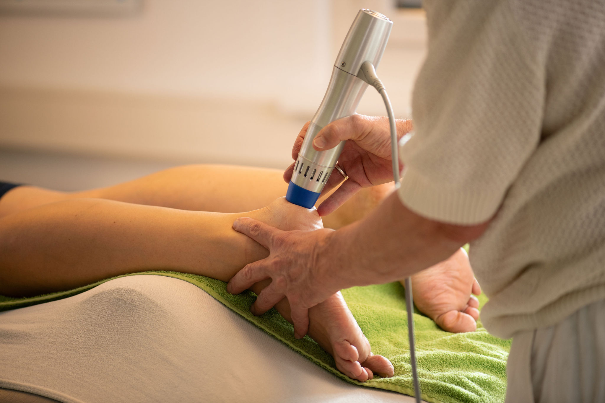 Physiotherapeut behandelt Patientenbein mit Stosswellentherapie Gerät in Physio Kinetic Fehraltorf